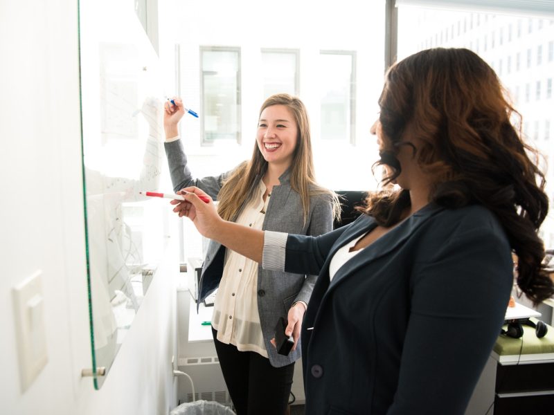 two women in front of dry erase board two women in front of dry erase board